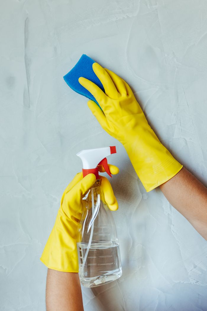 services-01 Hands in yellow gloves cleaning wall with sponge and spray bottle.
