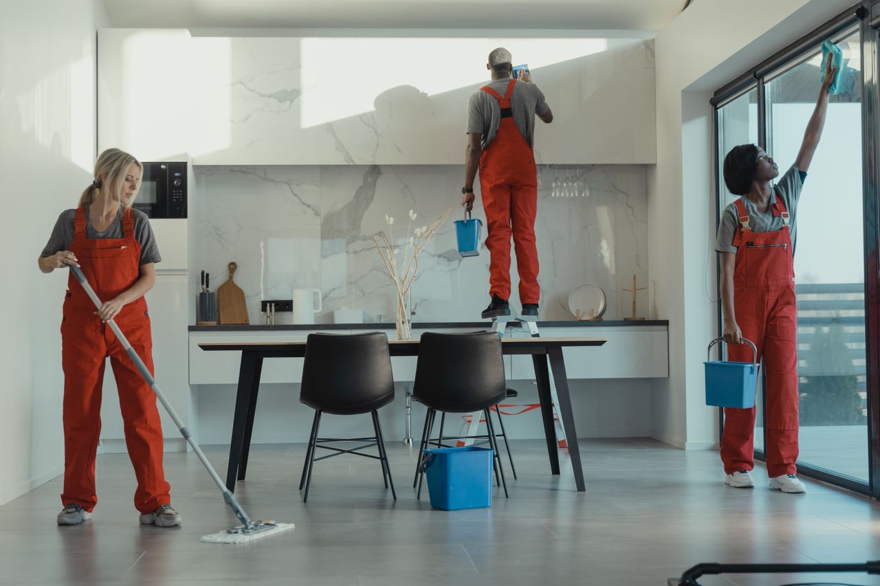 heros-img Group of cleaners in red uniforms mopping and wiping glass in a modern dining room.