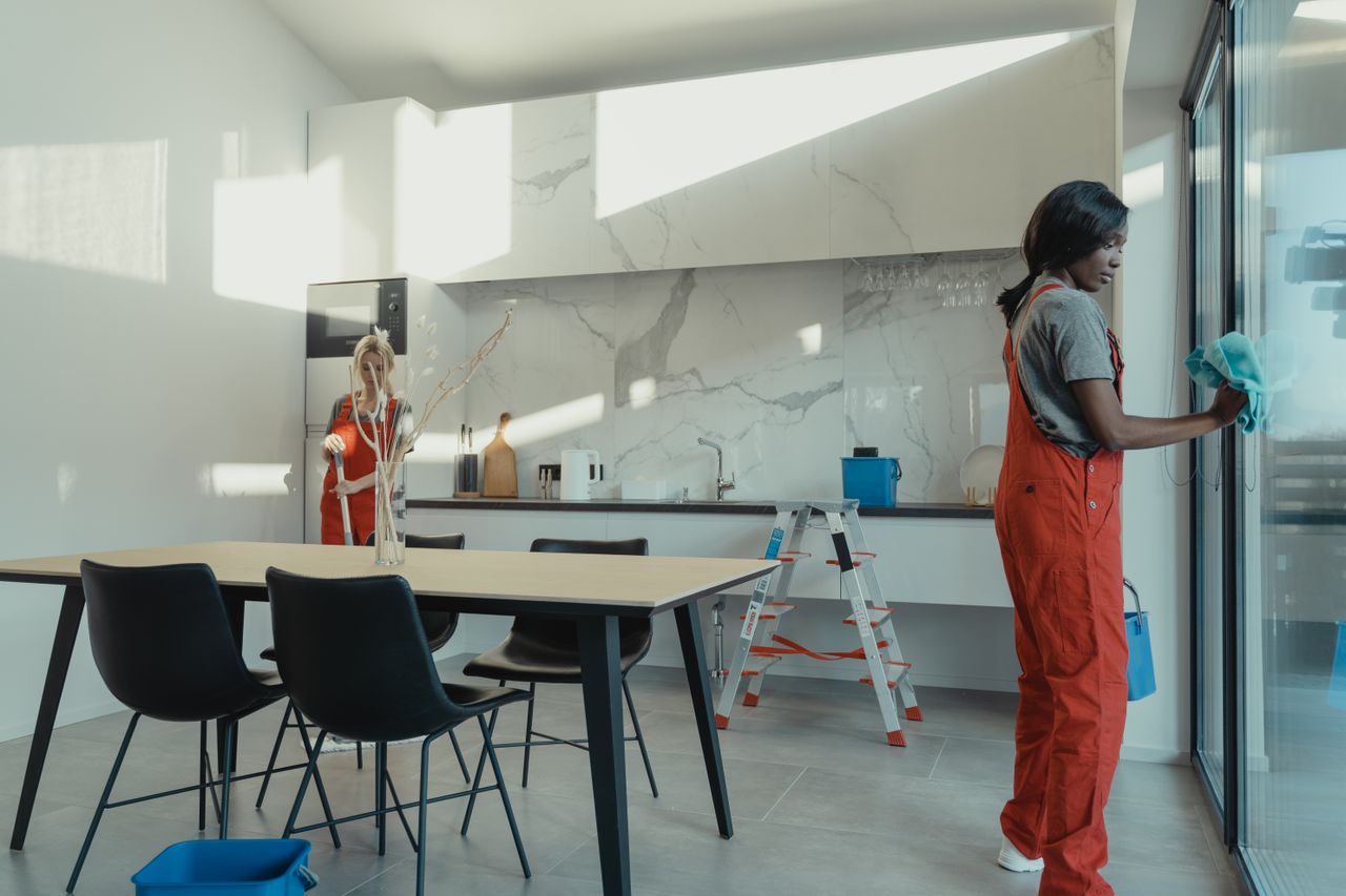 about-us Two women in work clothes cleaning a kitchen with glass doors.